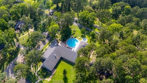 An aerial view of a property with a swimming pool, a tennis court, and a large lawn area surrounded by dense trees. - New Listing - Cape Royale Tree House w/ Fire Pit – Direct Lake Access (Coldspring)