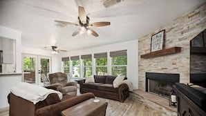 A living room with a fireplace, a ceiling fan, and a stone wall. - New Listing - Cape Royale Tree House w/ Fire Pit – Direct Lake Access (Coldspring)