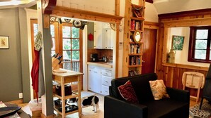 A cozy living room with a black sofa, a wooden dining table, and a kitchen in the background.