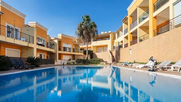 A swimming pool surrounded by multi-story buildings with balconies, a palm tree, and sun loungers. - Bright and modern 2 Bed Apartment in Vale de Parra (Guia)