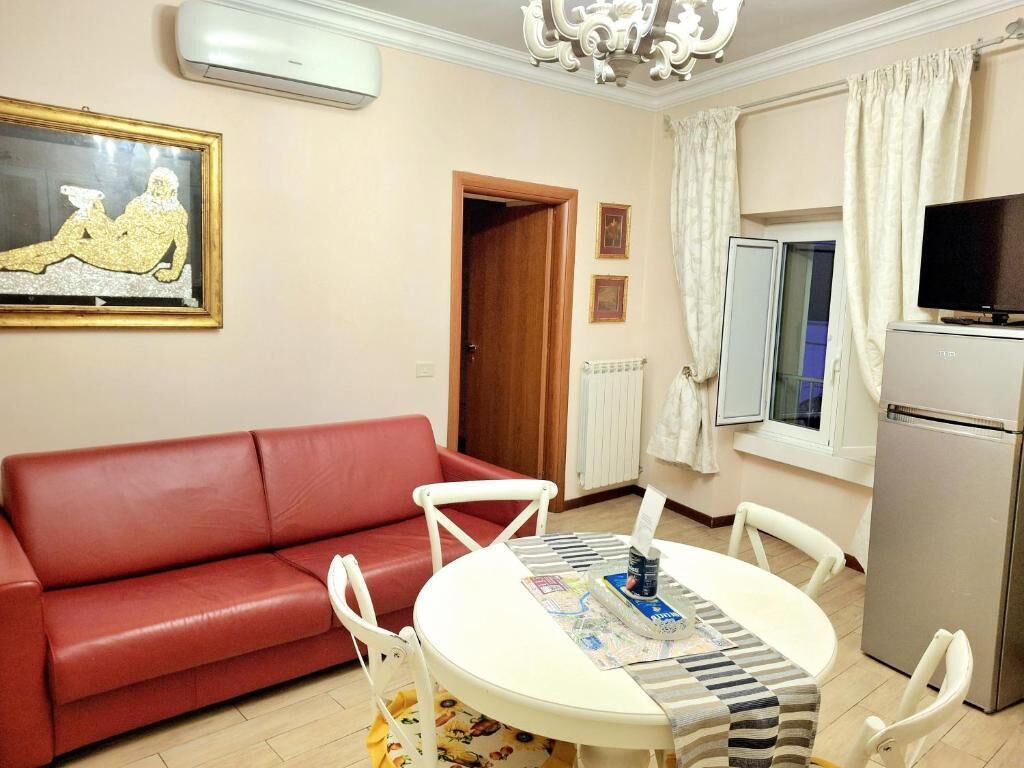 A living room with a red sofa, a round table with a striped tablecloth, a television, and a refrigerator.