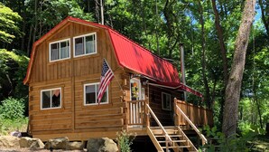 A wooden cabin with a red roof, a flag, and a staircase leading to a deck.