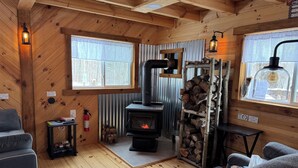 A cozy cabin interior with a wood-burning stove, a sofa, and a small table with books.