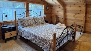 A wooden cabin bedroom with a bed, a nightstand, a chair, and a window.