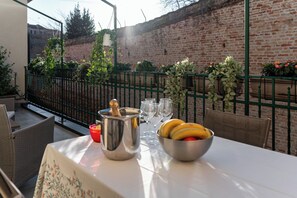 Une table dressée à l’extérieur, avec un pot en métal, un saladier de fruits et des verres à vin.