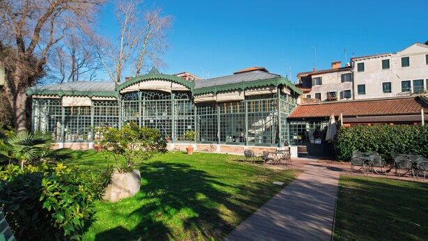 A conservatory with glass walls and a green roof, surrounded by a grassy area and a wooden deck.