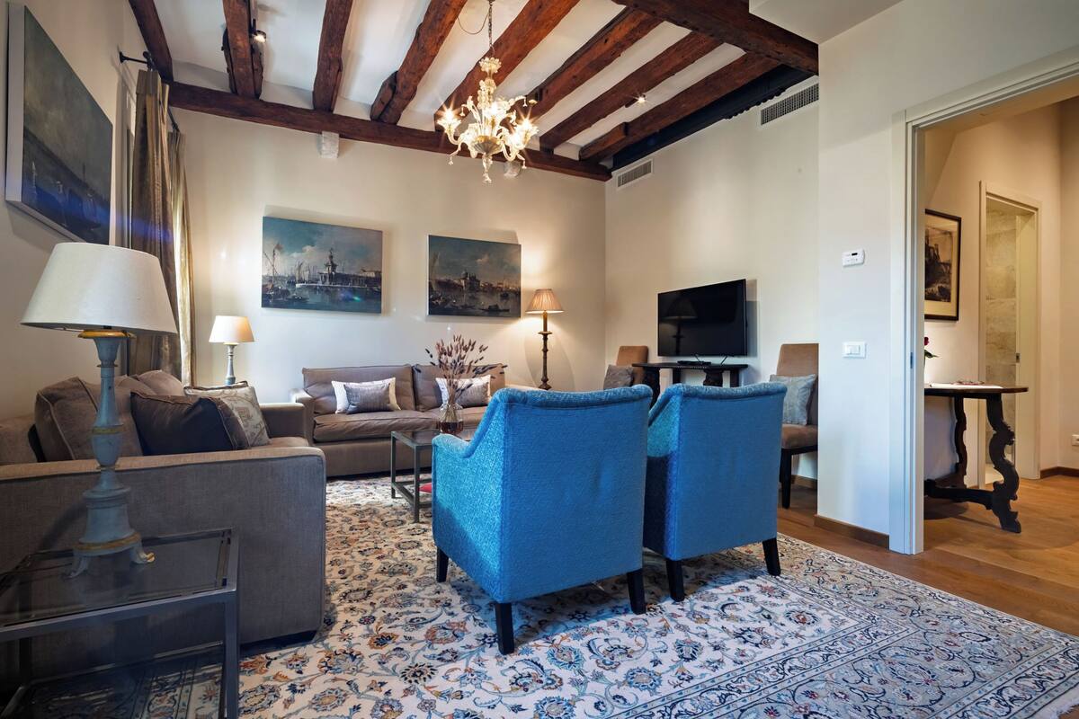 Un salon comprenant un canapé, deux fauteuils, un téléviseur et un lustre.