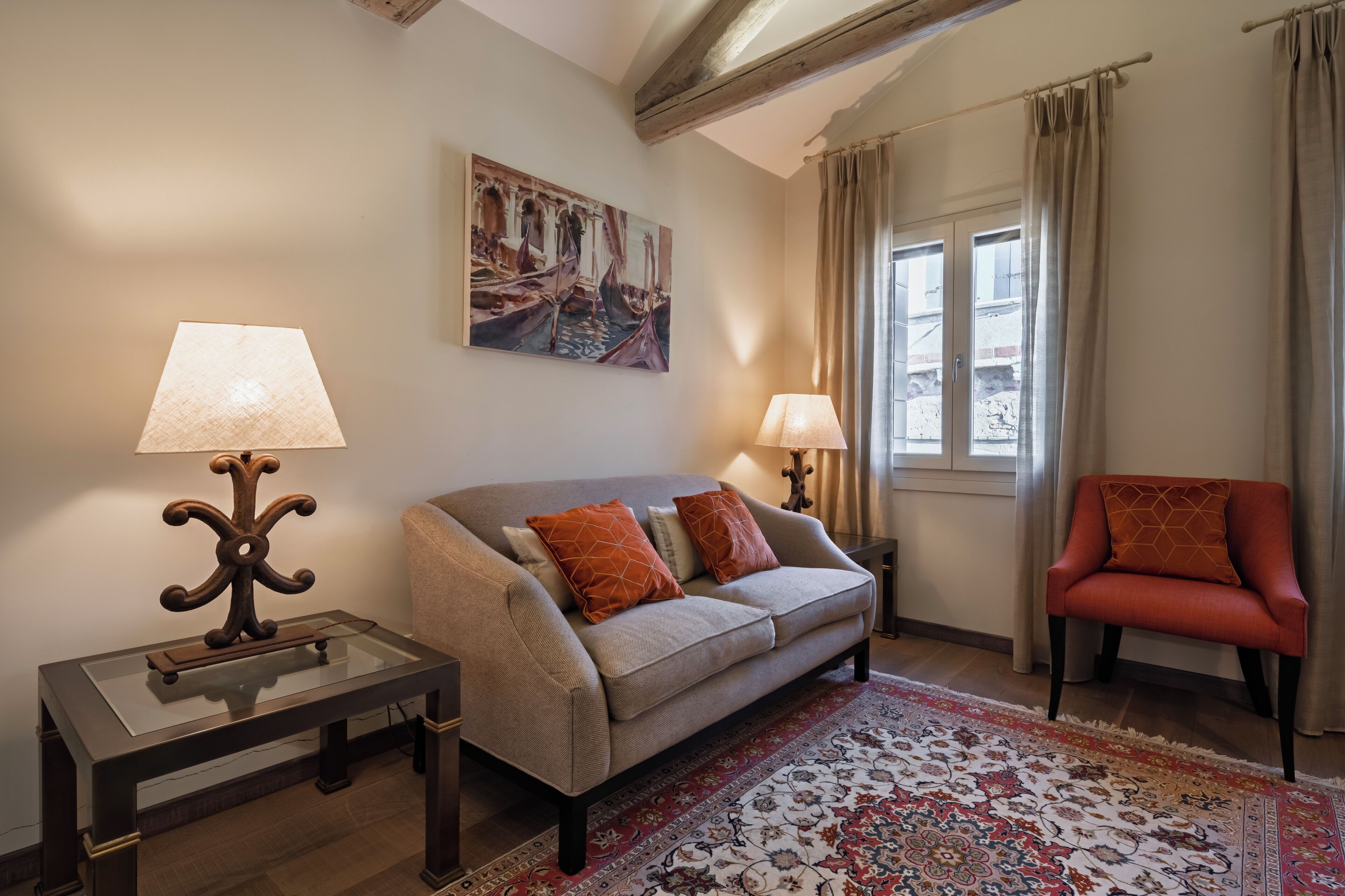 A living room with a sofa, two lamps, a chair, a rug, and a painting on the wall.