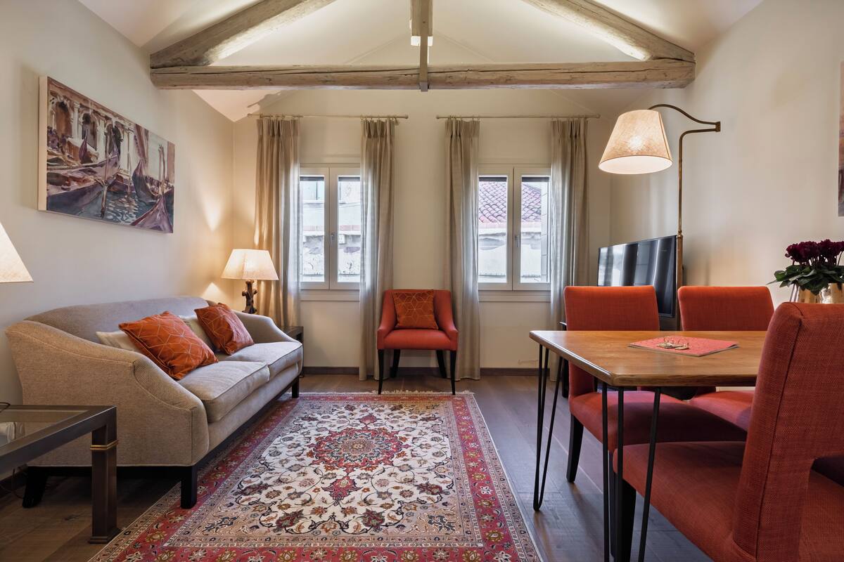 Un salon confortable avec un canapé, une table basse, une table à manger avec des chaises, un tapis et un tableau accroché au mur.