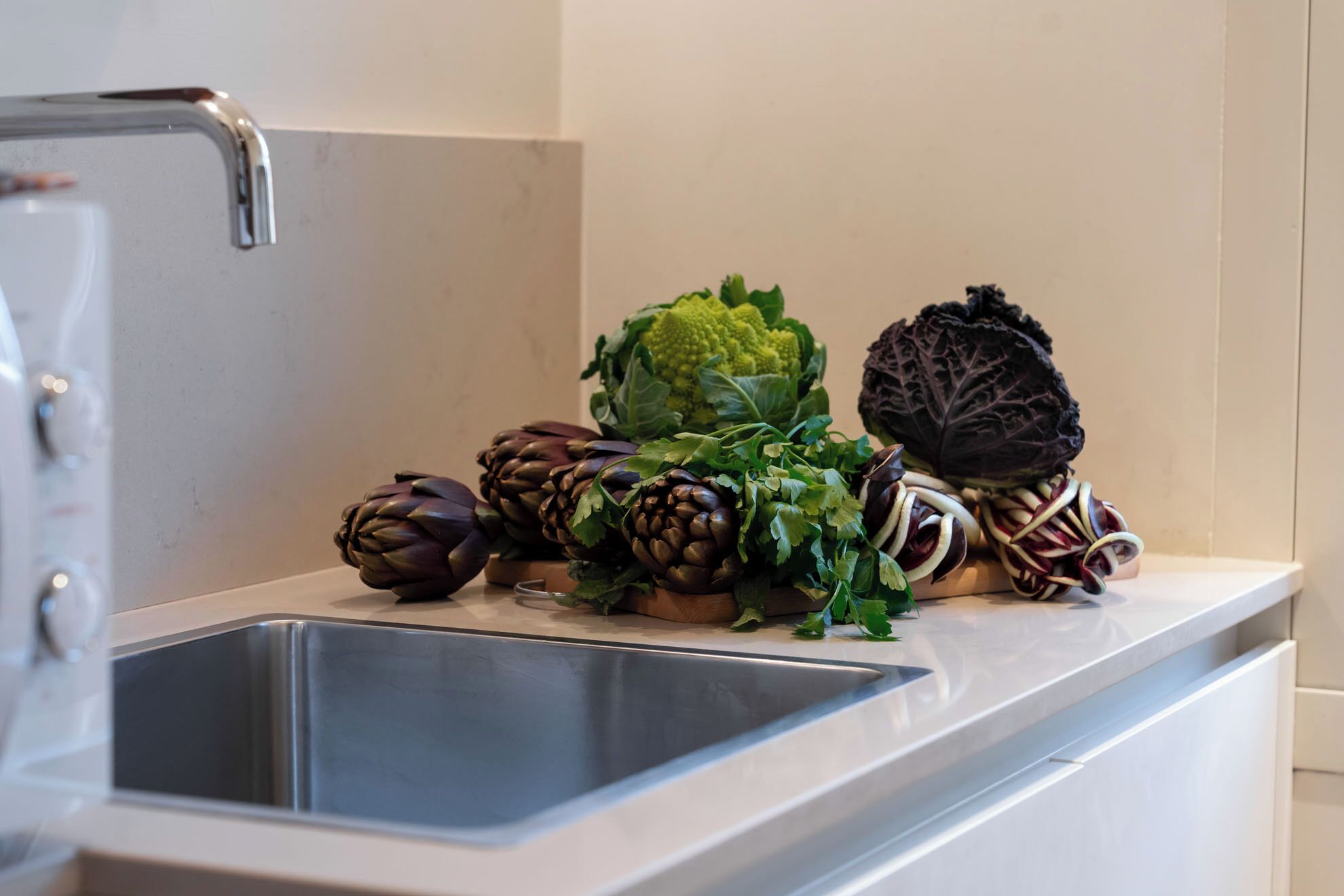 Uma bancada de cozinha com uma pia de aço inoxidável, diversos vegetais e uma torneira.