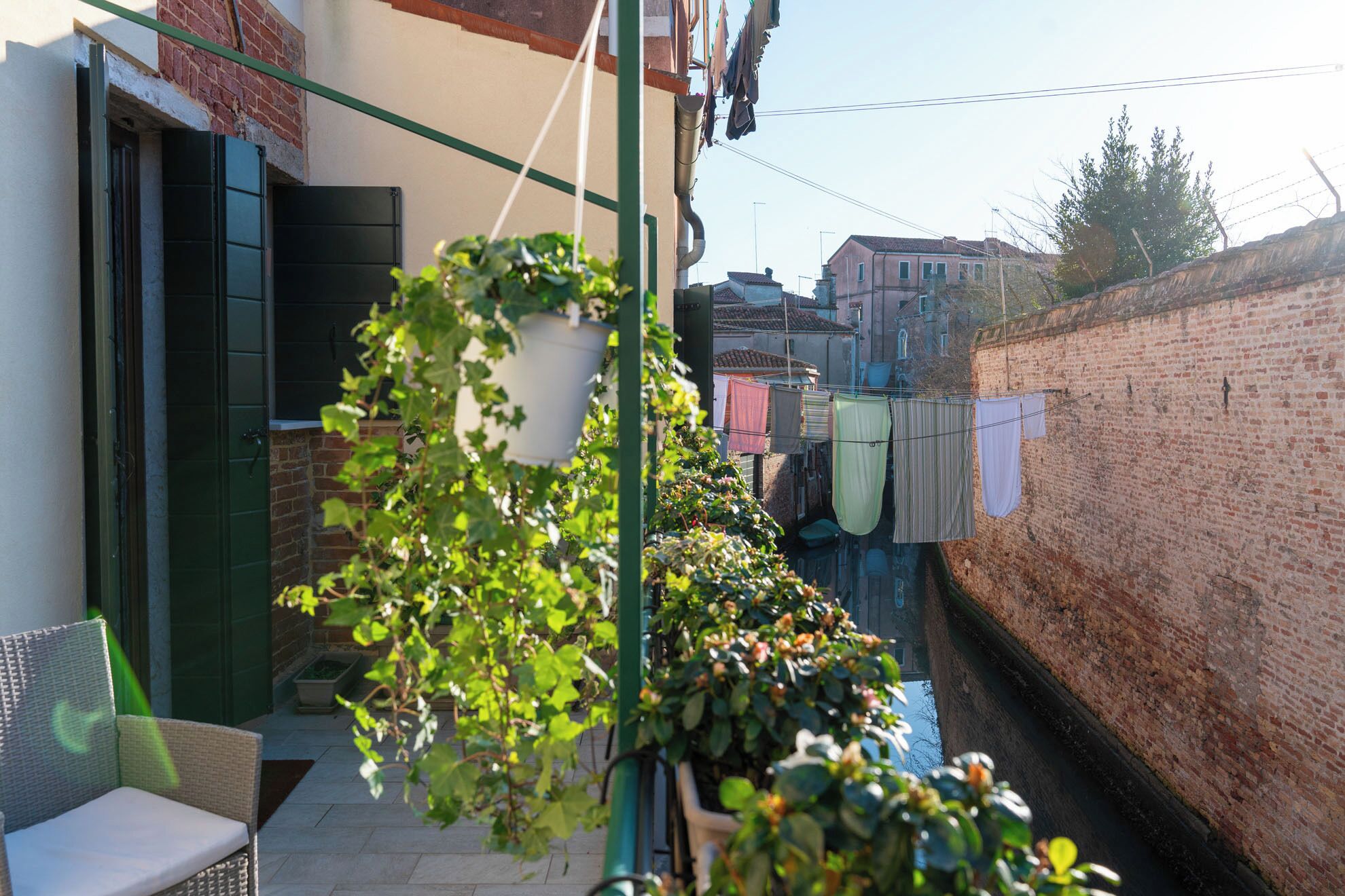 A narrow alleyway with a brick wall on one side and a building with a green door on the other. Clothes are hanging on a line.