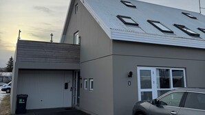 A modern building with a garage, a car parked in front, and a paved driveway. - Family house in Mosfellsbær (Mosfellsbær)