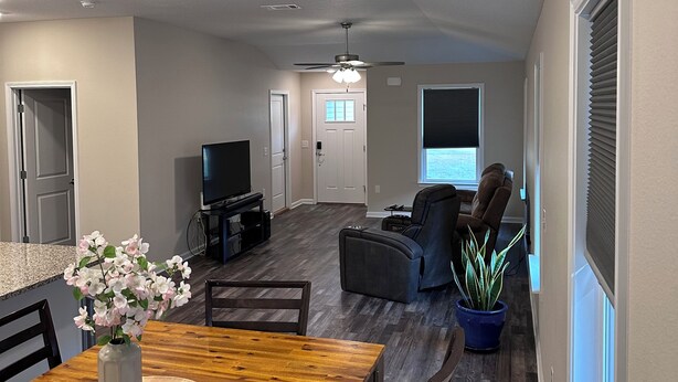 A spacious living room with a wooden dining table, a TV, and a ceiling fan. - Charming 3-bedroom 2-bath new build in the heart of crestview (Crestview)