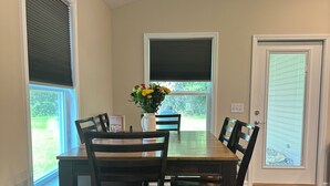 A dining area with a wooden table and four chairs, a vase with flowers, and a view of the outdoors through the windows. - Charming 3-bedroom 2-bath new build in the heart of crestview (Crestview)