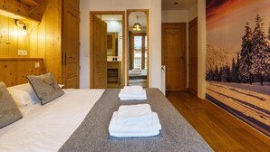 Een hotelkamer met houten wanden, een bed met witte lakens, een grijs vloerkleed en een schilderij van een besneeerd landschap.