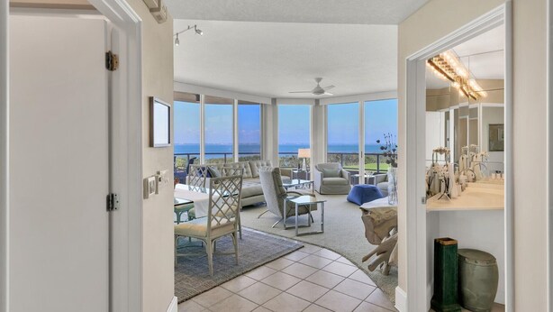 A spacious room with large windows offering a view of the sea, a ceiling fan, and a dining area with chairs and a table. - 2/2 Bay Front Condo, Pool, Private Beach Access (Longboat Key)
