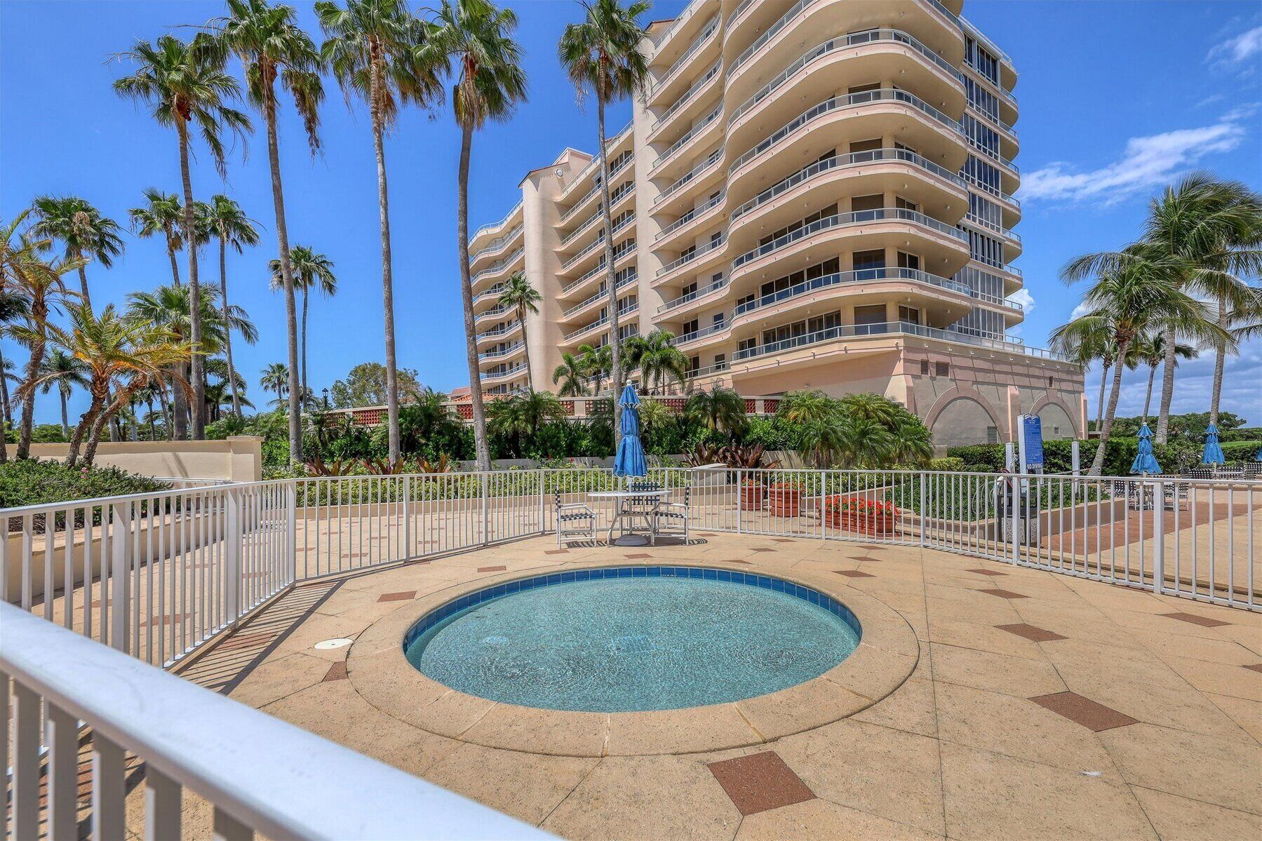 A hotel with a large pool, surrounded by palm trees and a white fence.