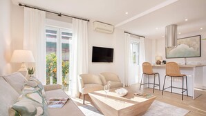 Una sala moderna con un sofá, dos sillones, una mesita de centro y un televisor. Hay un rincón comedor con dos sillas y una mesa.
