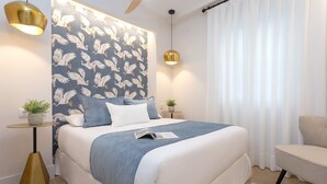 Un dormitorio moderno con una cama grande, un cabecero con diseño de papel tapiz texturizado, mesitas de noche con lámparas y una pequeña mesita con una planta.