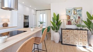 Una cocina moderna con una isla central, electrodomésticos integrados y un comedor con sillas de mimbre.
