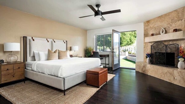Quarto com cama, mesas de cabeceira, ventilador de teto, lareira e vista para o exterior.