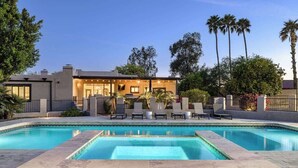 Uma casa moderna com piscina, cadeiras de descanso e palmeiras.