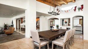 Uma sala de jantar ampla com uma grande mesa de madeira, várias cadeiras e um lustre.