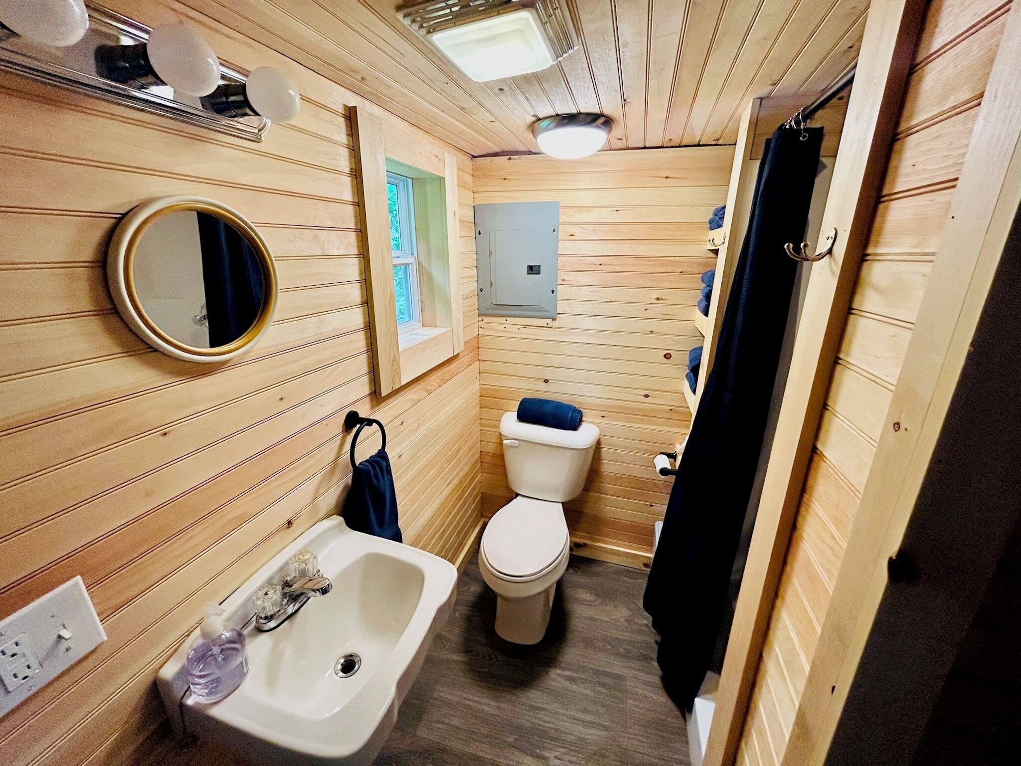 Ein kleines Badezimmer aus Holz mit Waschbecken, Toilette und Spiegel.