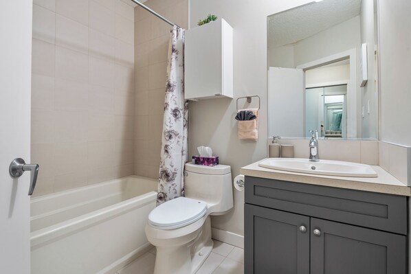 A bathroom with a toilet, shower, sink, and mirror.