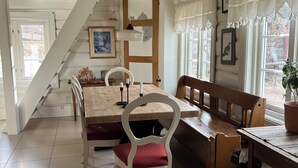 A dining area with a wooden table, white chairs, and a bench. A staircase leads to another room. - Old log cabin from 1830 with soul. (Trøndelag)