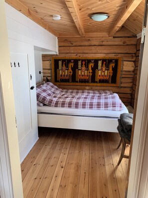 A wooden cabin room with a bed, a wall tapestry, and a wooden floor. - Old log cabin from 1830 with soul. (Trøndelag)