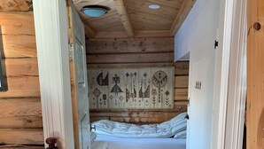A wooden cabin room with a bed, a chair, and a door with a number. - Old log cabin from 1830 with soul. (Trøndelag)