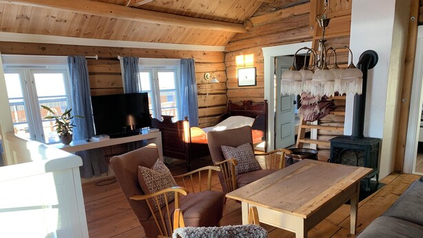 A cozy cabin interior with a wooden floor, a TV, a dining table, and a sofa. - Old log cabin from 1830 with soul. (Trøndelag)