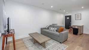A modern living room with a grey sofa, wooden coffee table, and a TV on a wooden stand. - Capitol Hill Suites - Unit 3 (Washington)