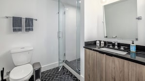 A modern bathroom with a glass-enclosed shower, a white toilet, and a wooden vanity with a black countertop. - Capitol Hill Suites - Unit 3 (Washington)