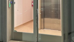 En modern hiss med en glasdörr, ett digitalt knappsats och en brandsläckare som är monterad på väggen.