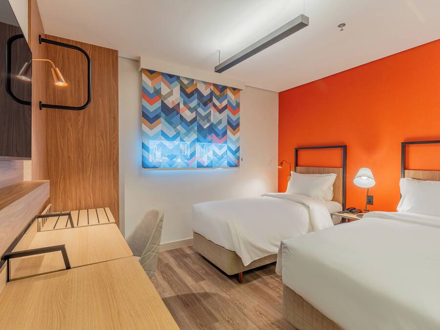 Une chambre d’hôtel moderne avec deux lits, un bureau et une œuvre d’art abstraite et colorée au mur.