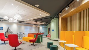 A modern lounge area with seating arrangements, including red chairs, green sofas, and yellow couches. There are tables and a hanging chair.