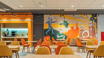 A dining area with tables and chairs, a mural with cultural artwork, and a counter with a coffee machine.