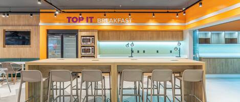 A breakfast area with a long counter and bar stools, equipped with a microwave and refrigerator.
