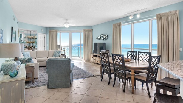 A spacious living room with a large window overlooking the ocean, a dining area with a wooden table and chairs, and a cozy seating area with a sofa and armchairs. - Drastic Reduction for Labor Day! Gulf front, updated, Pool, Hot Tub plus Gym. (Destin)