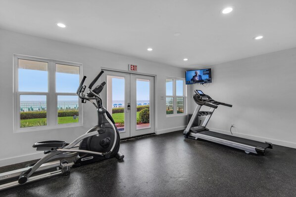 A gym with two treadmills, a stationary bike, and a TV screen.