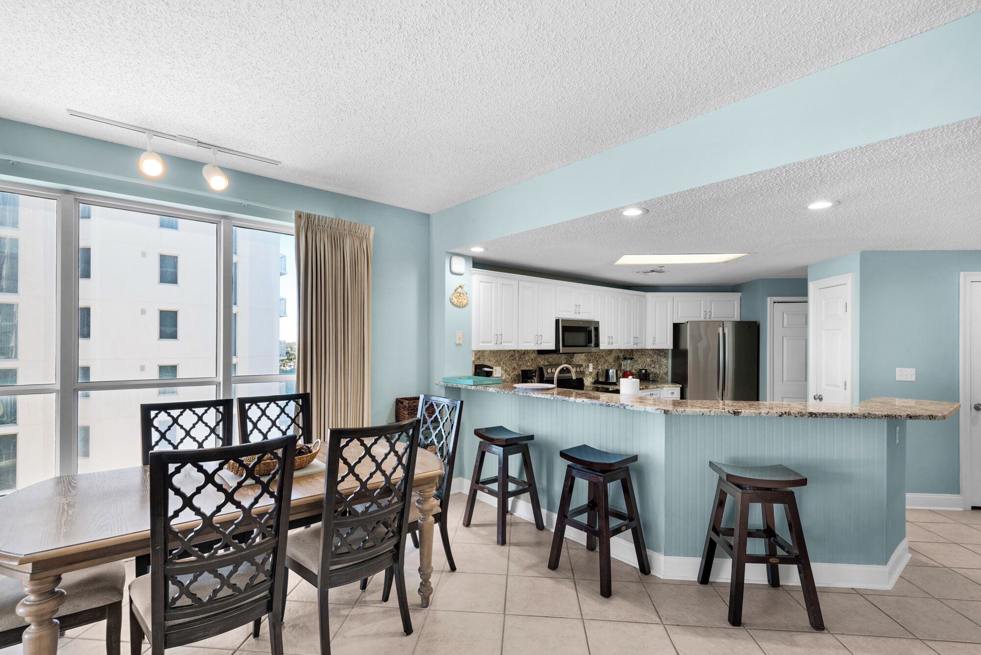 A modern kitchen with white cabinets, a granite countertop, and stainless steel appliances. There is a dining area with a wooden table and chairs.