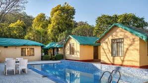 A pool area with tiled flooring, a pool with clear blue water, and two white wicker chairs. - The Wild Orchid Resort (Ramnagar)