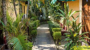 A narrow pathway flanked by lush greenery and a building with a green roof. - The Wild Orchid Resort (Ramnagar)