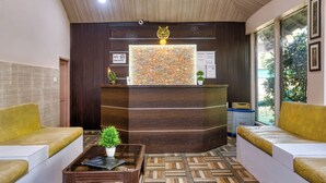 A reception area with a stone wall, a tiger statue, and two yellow sofas. - The Wild Orchid Resort (Ramnagar)