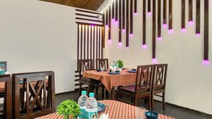 A dining area with wooden chairs, a table with a red and white checkered tablecloth, and a wall with vertical wooden slats and purple lights. - The Wild Orchid Resort (Ramnagar)