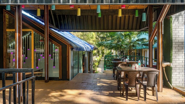 An outdoor seating area with tables and chairs, a covered walkway, and a view of the surrounding greenery. - The Wild Orchid Resort (Ramnagar)