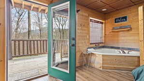 Interior de una cabaña de madera con un amplio ventanal corredero que da a una terraza, una bañera y un cartel que dice 'Relax'.