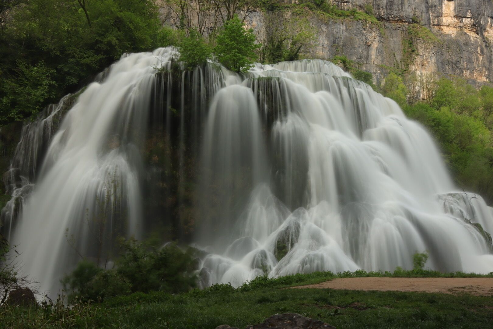 Ein Wasserfall stürzt über eine felsige Klippe, umgeben von üppiger Vegetation.